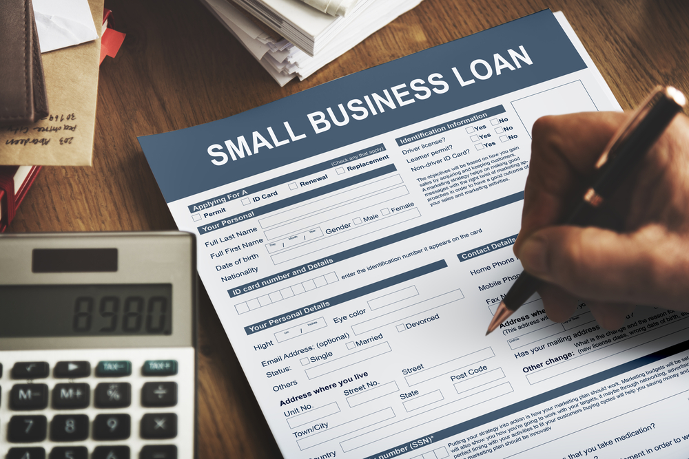 hand of a man filling up a small business loan form with calculator